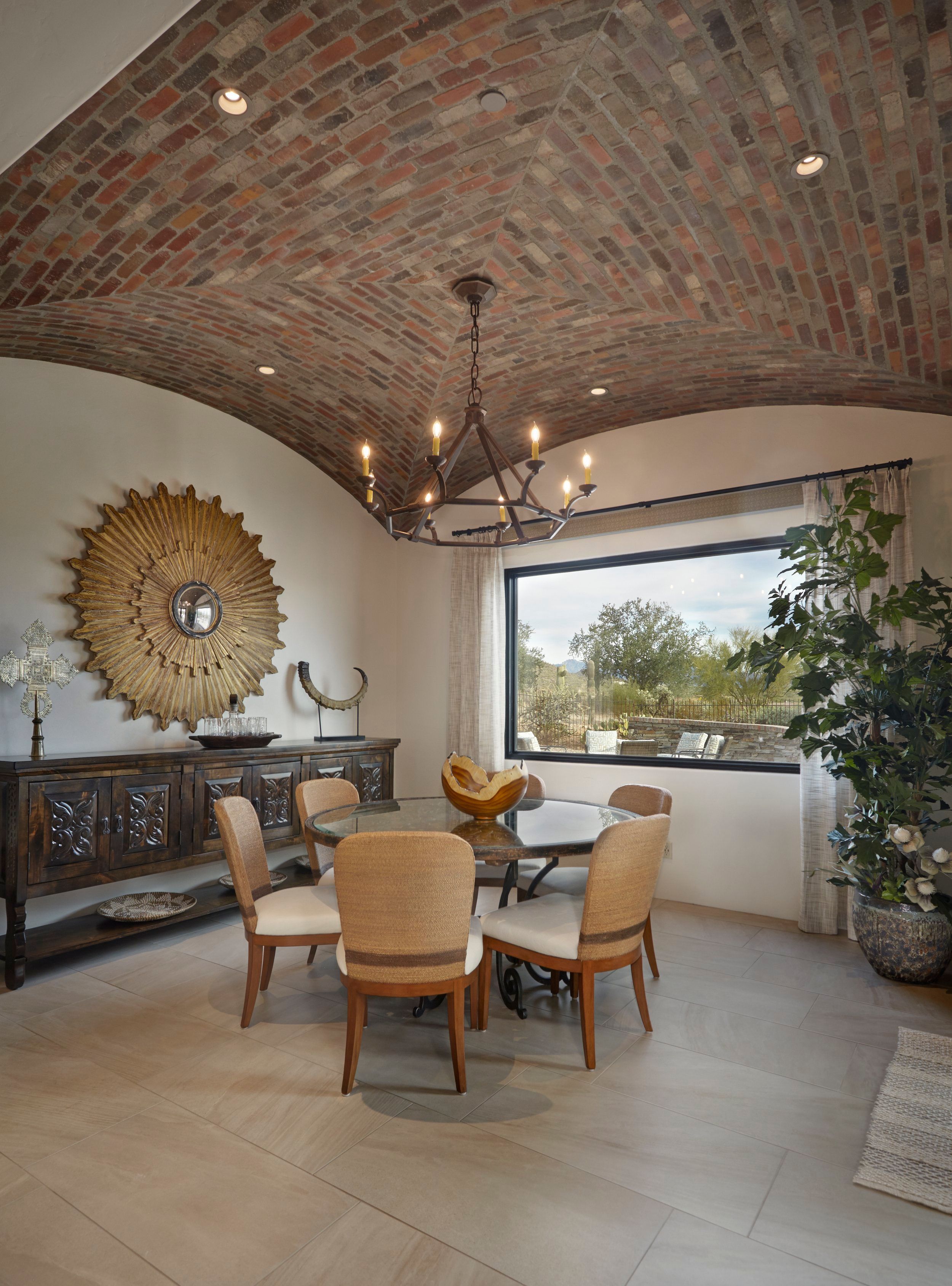 Dining room beneath a barrel-vaulted brick ceiling with an iron chandelier and sunburst mirror