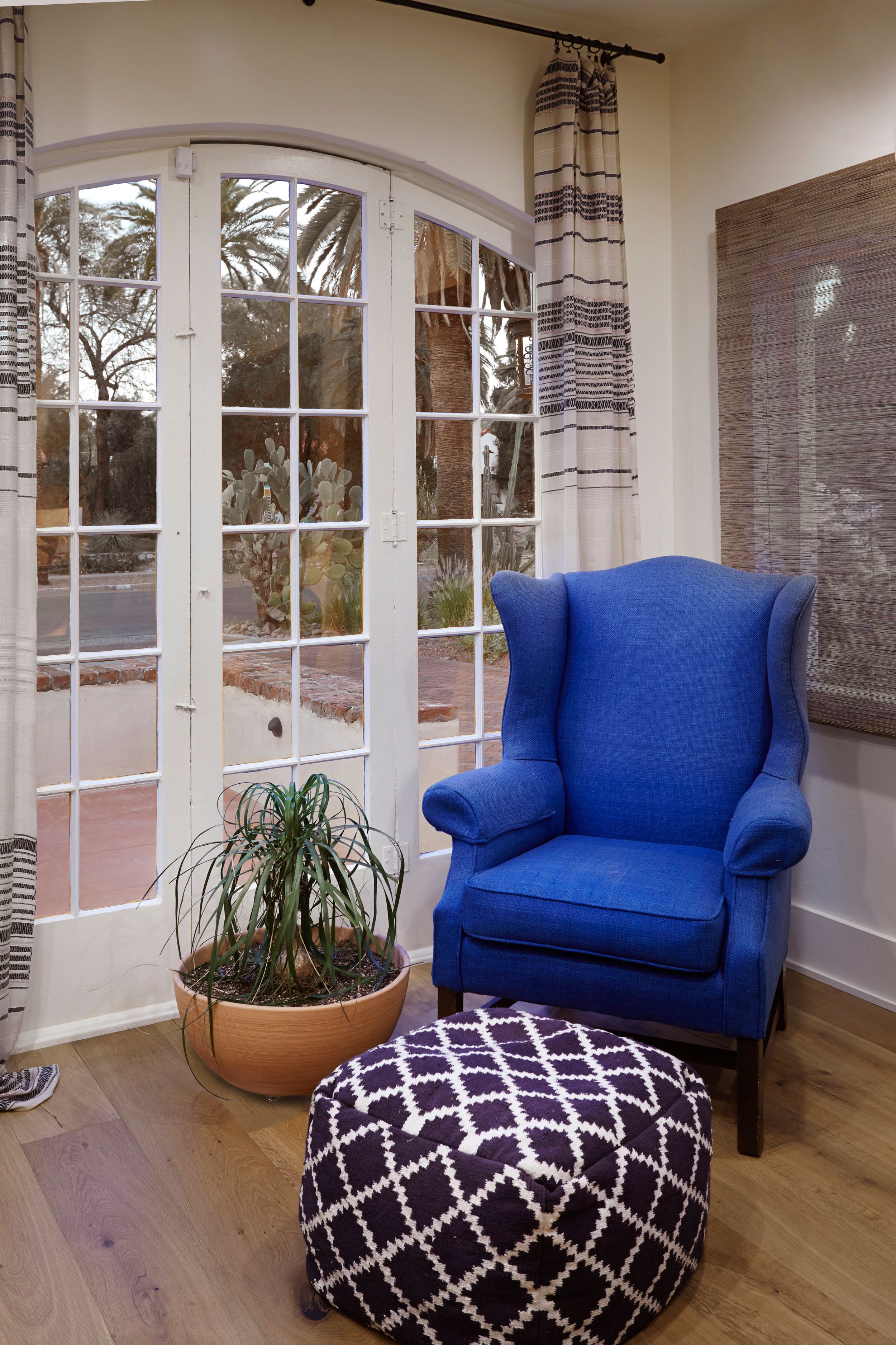 Blue wingback chair beside arched French doors with a patterned ottoman