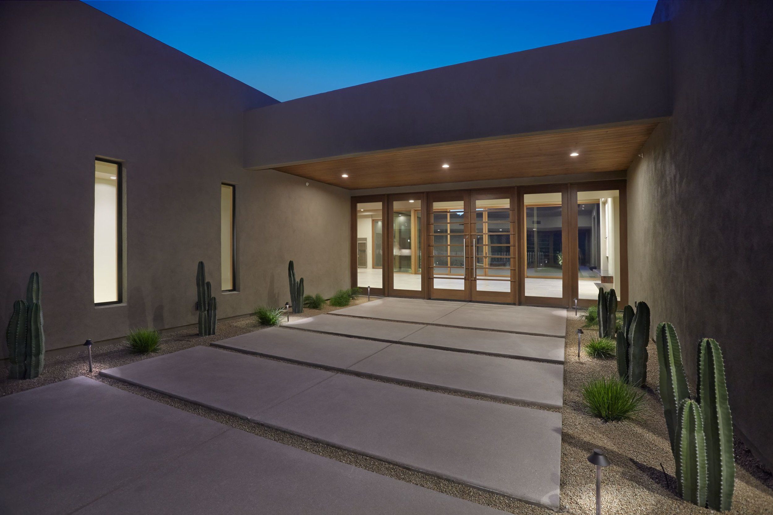 Entry courtyard with tall cacti, concrete paving and glass entry doors