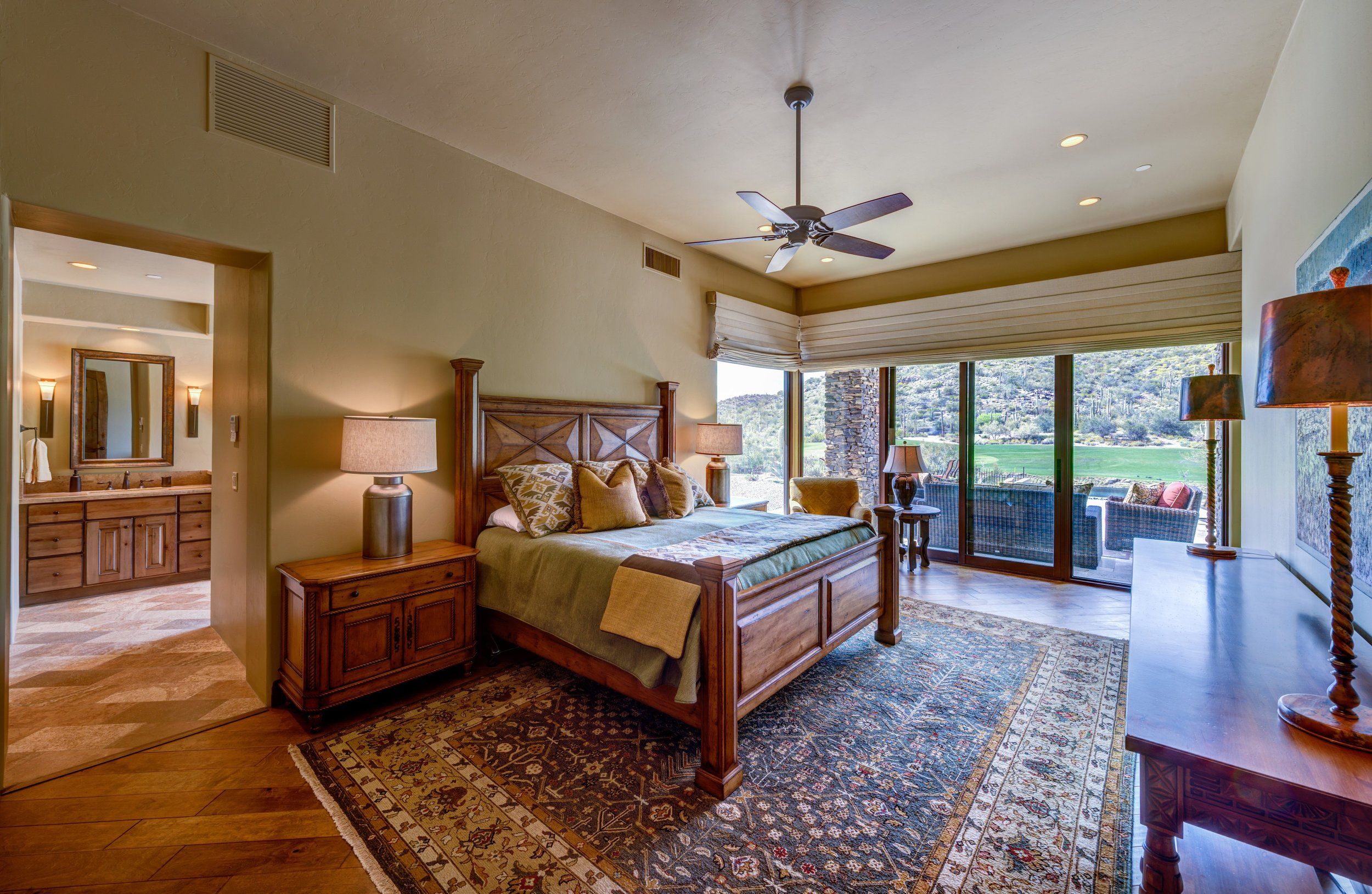 Primary bedroom with a carved wood bed, ceiling fan and ensuite beyond