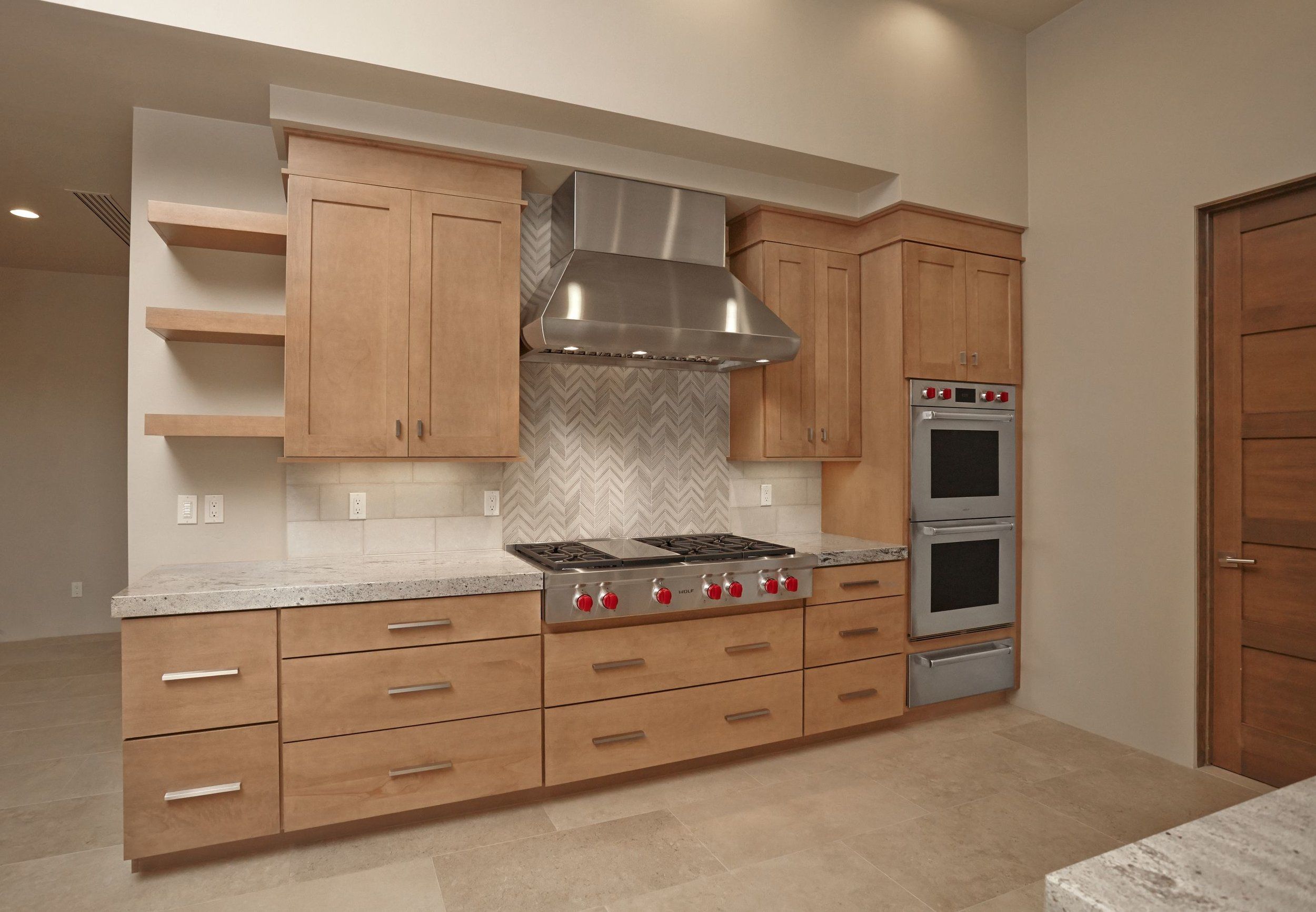 Cooktop wall with a stainless hood, herringbone backsplash and double wall ovens