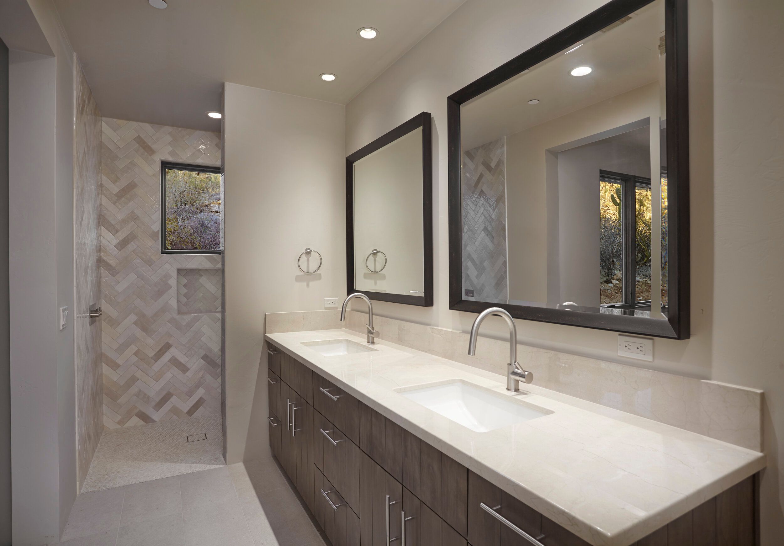 Guest bathroom with twin vanities, framed mirrors and a herringbone-tiled shower