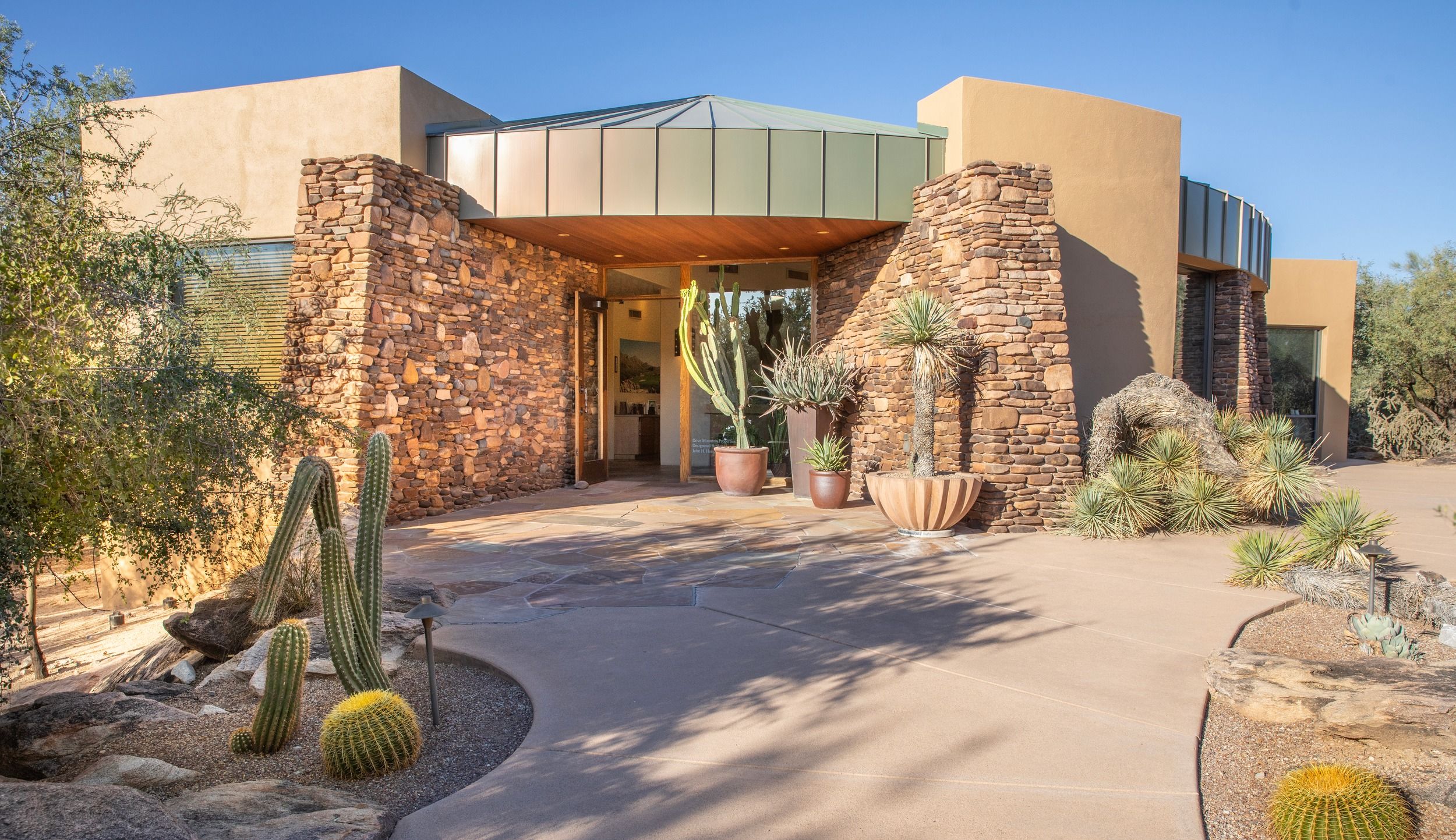 Dove Mountain Homes office entrance with stone columns, a copper-toned canopy, and native desert landscaping